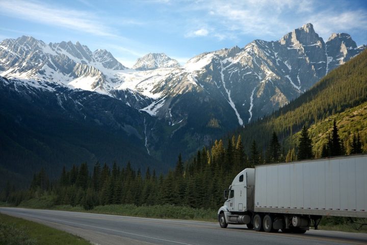 An image of a trailer truck on the road near  forests and mountains